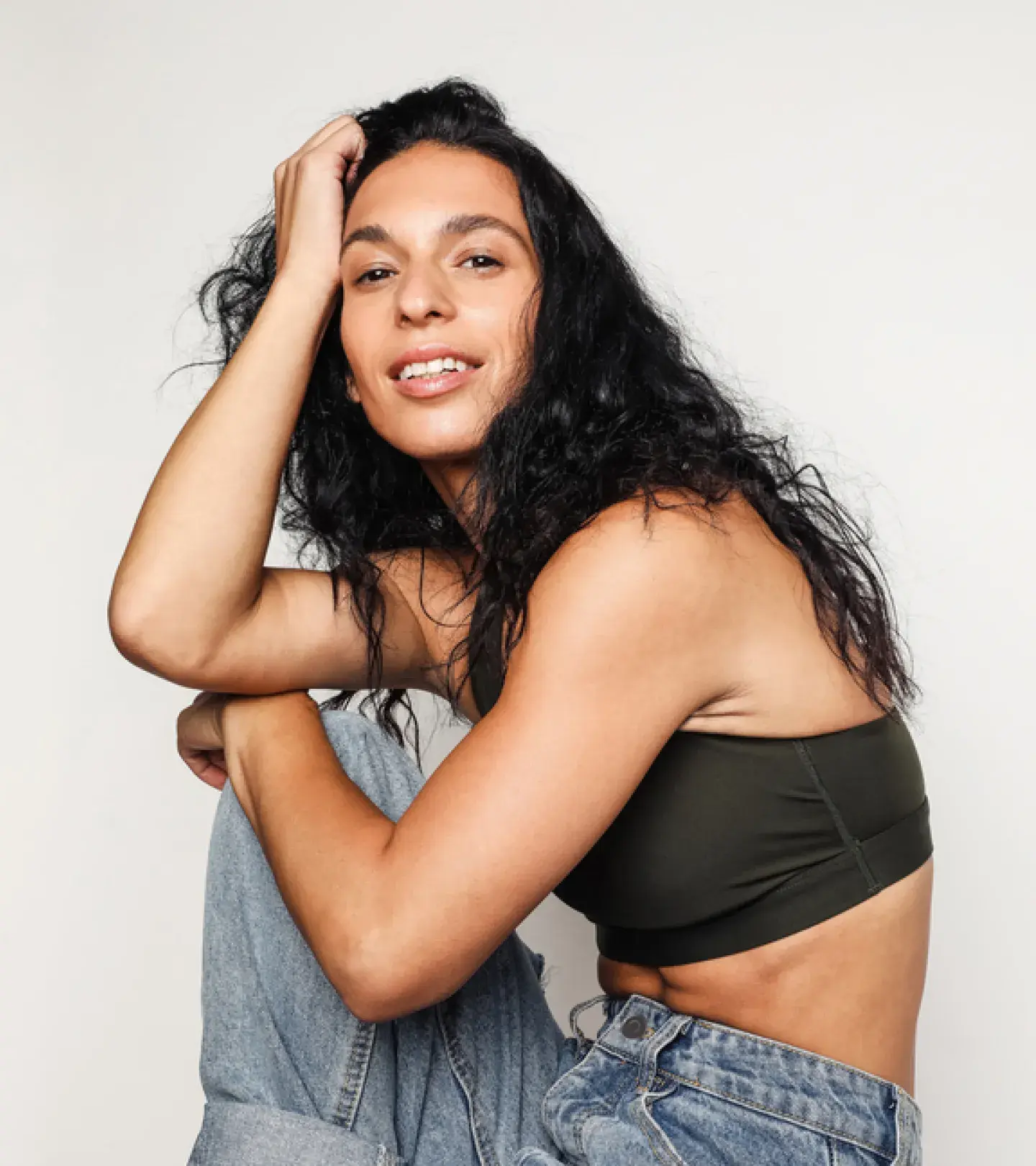 An image of a woman with dark, long hair sitting and leaning on her knee