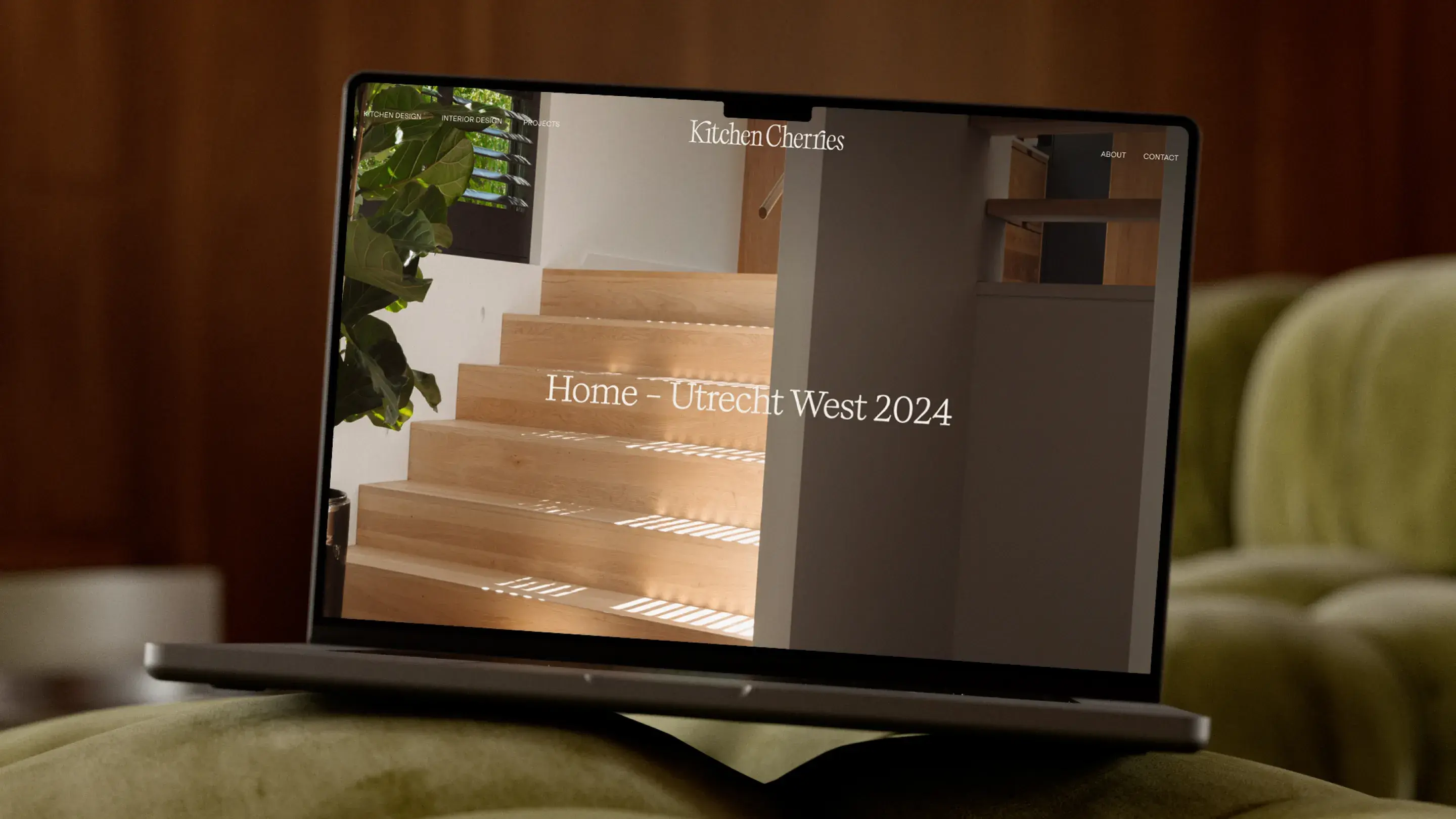 Laptop displaying a website with a wooden staircase image, titled "Home - Utrecht West 2024," on a green cushioned surface.
