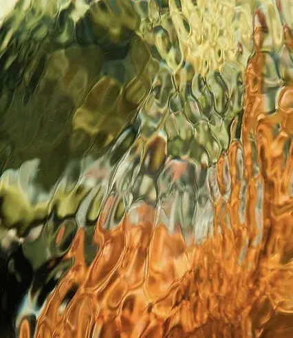 Abstract image featuring swirling patterns with green, yellow, and orange hues, creating a textured, fluid appearance reminiscent of rippling water.
