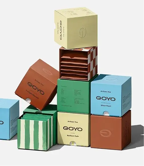Stacked colorful tea boxes with minimalist designs, featuring checkered, striped, and solid patterns. Labeled "GOYO Artisan Tea."